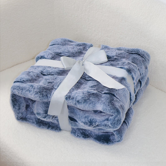 A folded soft blue plush blanket with a velvety texture, secured by a silver-gray satin ribbon tied into an elegant bow at the center. The clean light background creates a gentle contrast, emphasizing the blanket's cozy quality and refined presentation.