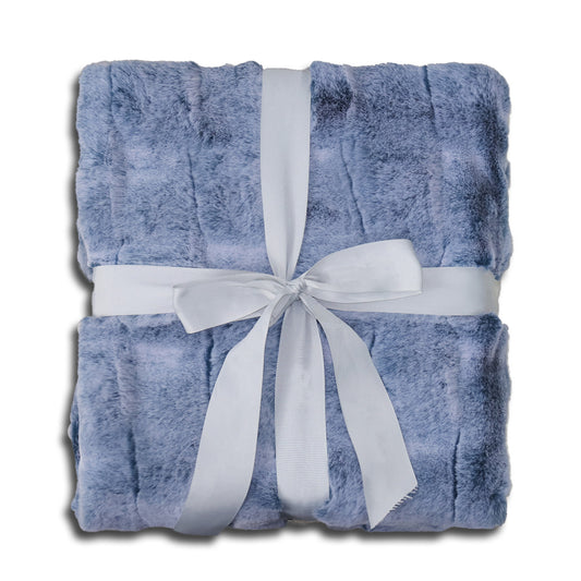 A folded soft blue velvet blanket with subtle surface texture, elegantly decorated with a white ribbon tied into a bow at the center. The clean white background highlights the harmonious blue-and-white color palette, evoking a sense of calmness, warmth, and timeless elegance.