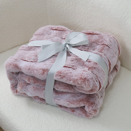 A folded soft pink plush blanket with a fluffy texture, elegantly wrapped with a silver-gray satin ribbon tied into a bow at the center. The clean light fabric background creates a harmonious contrast, emphasizing the blanket's warmth and the ribbon's sophisticated detailing, suitable for gift presentation or cozy home decor.