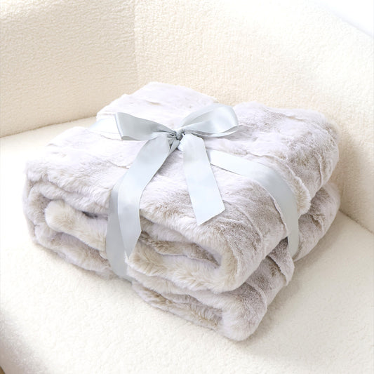 A stack of soft gradient-gray plush blankets tied with a silver-gray satin ribbon bow. The velvety texture and light gray-to-white color transition create a cozy aesthetic, complemented by a soft fabric background. The minimalist composition emphasizes the blankets' luxurious feel and versatile home decor appeal.