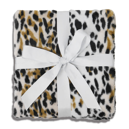 Square faux-leopard print throw pad in ivory with irregular black and caramel spots, featuring a plush polyester velvet surface. Central white satin bow adds elegant contrast. Displayed on pure white background, emphasizing symmetry and tactile texture.