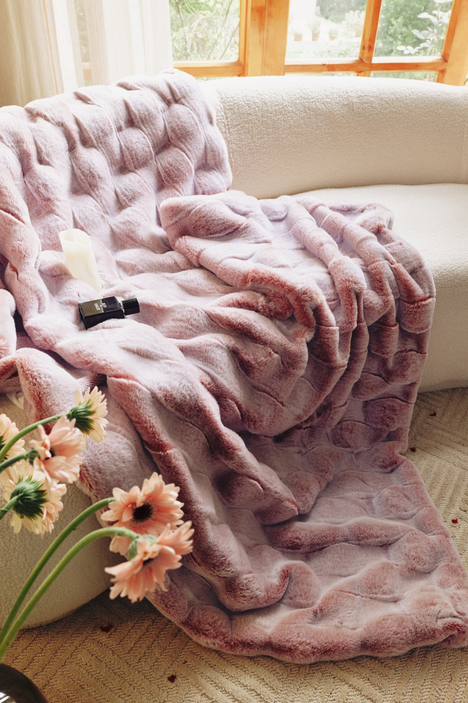 A plush gradient blanket in soft pink tones, transitioning from blush to rose, featuring a cloud-like fur texture and scattered silk petals, evoking a romantic bedroom oasis.