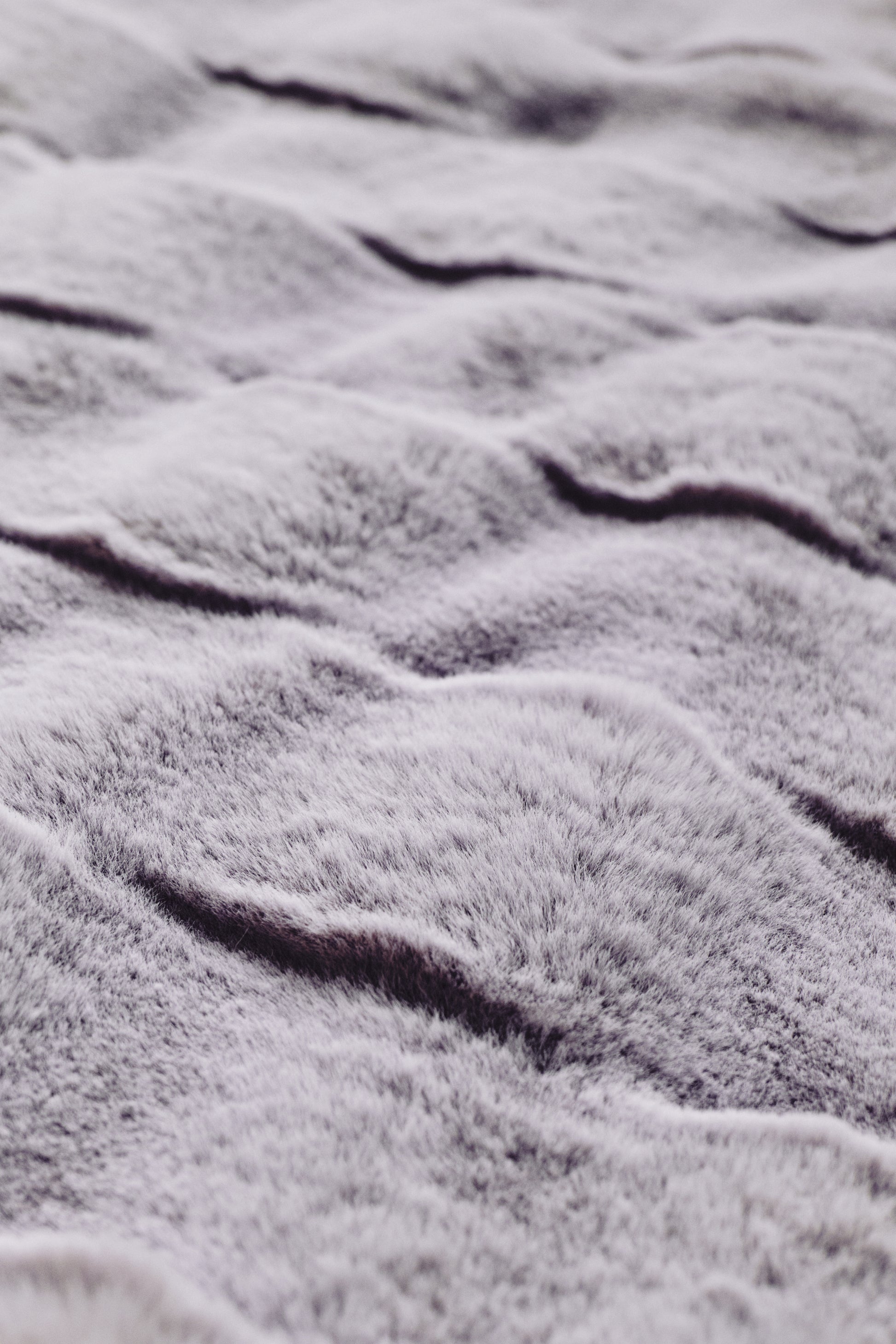 A luxurious purple throw with a smooth gradient from rich plum to blush tones, showcasing a plush, velvety texture and subtle wavy embossing, radiating serene sophistication.