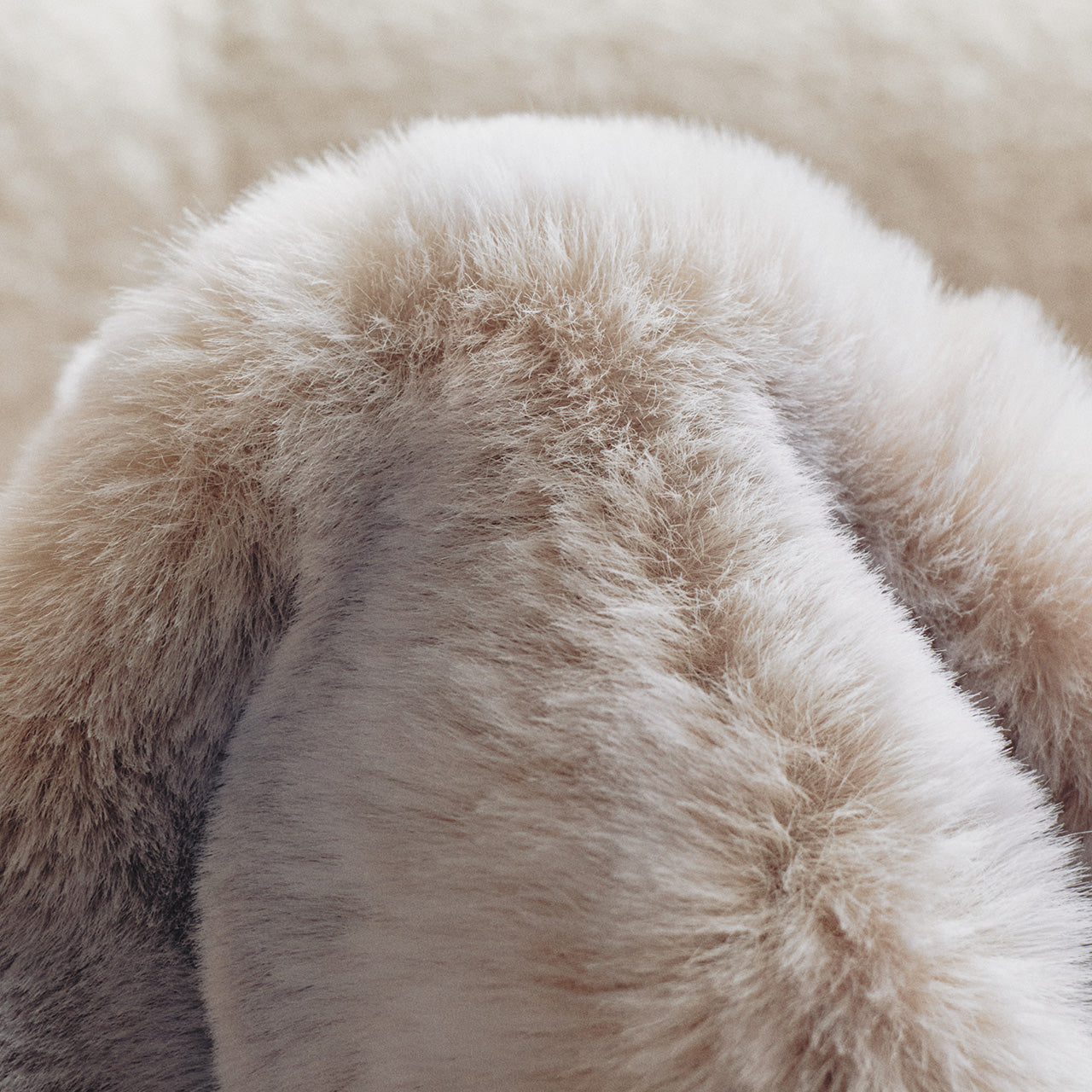 A cozy beige throw with soft gradient hues and a luxuriously fluffy fur texture, radiating understated warmth in its uncluttered design.