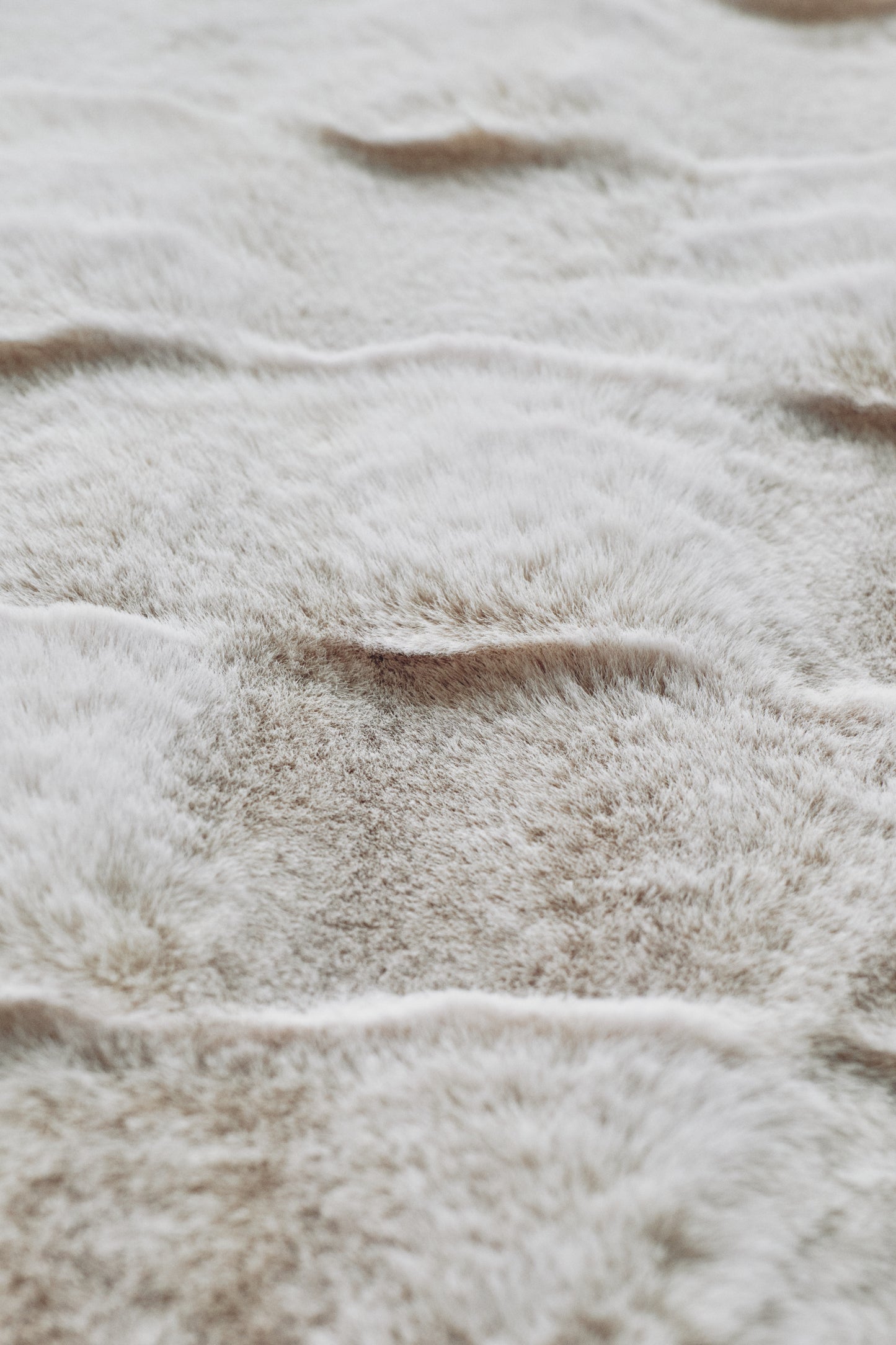 A plush beige blanket with seamless color gradations and a fur-like texture, embracing minimalist elegance through its unadorned, natural aesthetic.