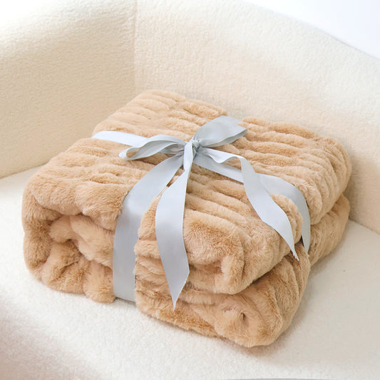 A folded beige textured blanket tied with a light gray ribbon rests on a white, plush surface.