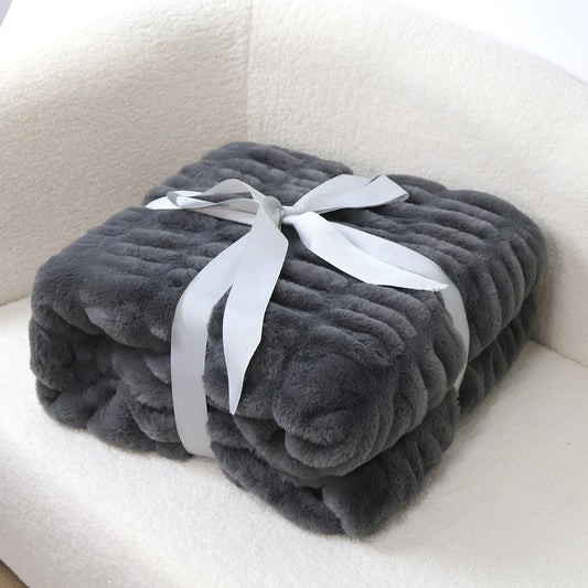 A folded dark gray plush blanket with ribbed texture is tied with a light gray satin ribbon on a white fluffy surface.