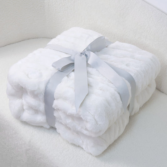 A neatly folded white plush blanket secured with a light gray ribbon on a white textured surface.