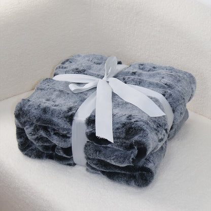 A rolled gray plush blanket with a soft, fluffy texture, secured with a white satin ribbon tied into an elegant bow at the top. The clean light background creates a subtle contrast with the blanket's neutral tone, emphasizing its cozy quality and refined presentation.