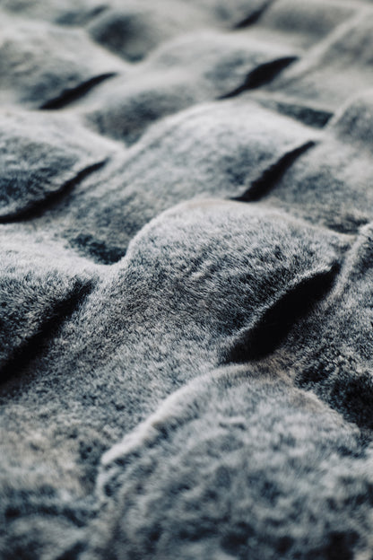 A dramatic gradient blanket in deep obsidian hues, textured with undulating 3D waves and a matte-sheen finish, ideal for contemporary interiors.