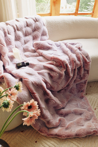 A plush gradient blanket in soft pink tones, transitioning from blush to rose, featuring a cloud-like fur texture and scattered silk petals, evoking a romantic bedroom oasis.