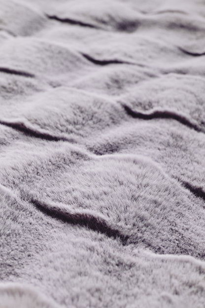 A luxurious purple throw with a smooth gradient from rich plum to blush tones, showcasing a plush, velvety texture and subtle wavy embossing, radiating serene sophistication.
