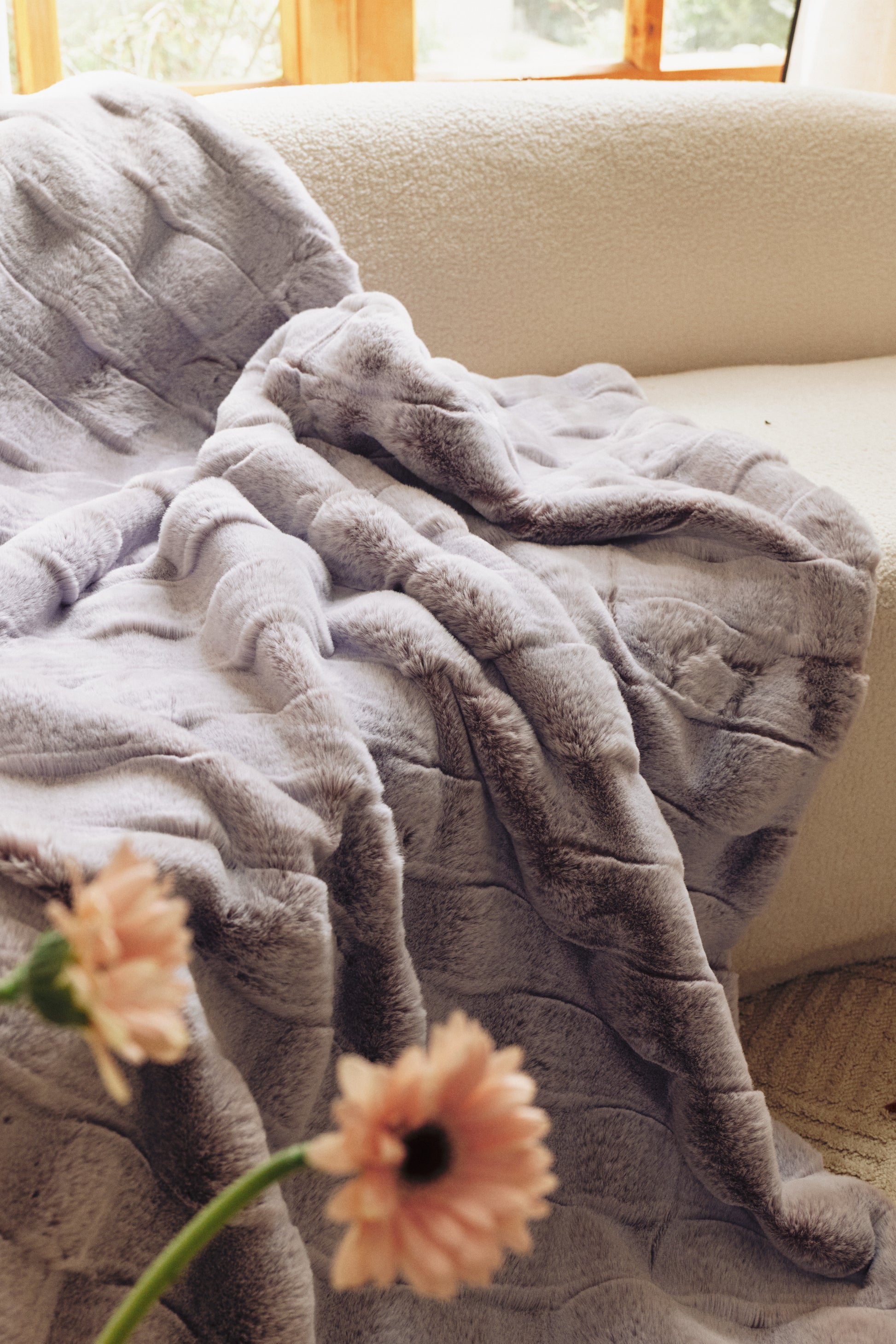 A quilted purple blanket draped over a sofa, featuring a soft gradient from deep violet to lavender, textured stitching, and delicate pink floral accents for a cozy, elegant vibe.