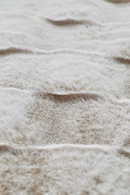 A plush beige blanket with seamless color gradations and a fur-like texture, embracing minimalist elegance through its unadorned, natural aesthetic.