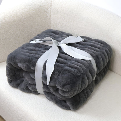A folded dark gray plush blanket with ribbed texture is tied with a light gray satin ribbon on a white fluffy surface.