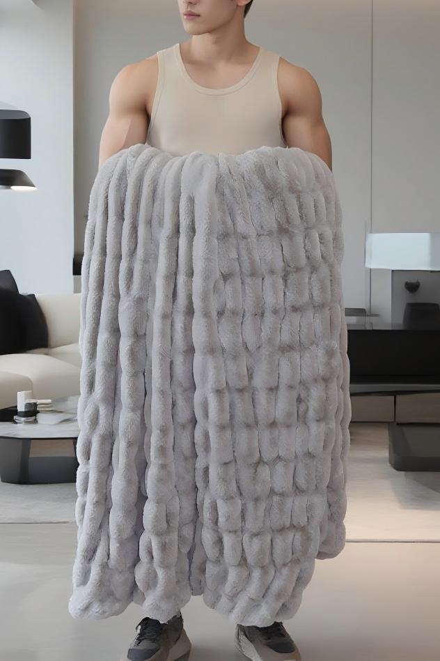 A person in a beige tank top holds a textured gray blanket with a braided pattern in a modern living room.