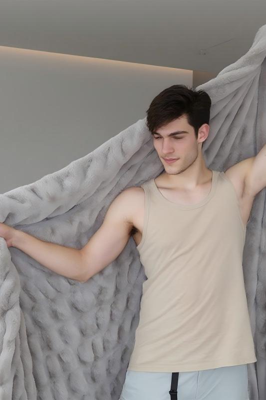 A man in a beige tank top holds a textured gray fabric against a plain wall with ceiling lighting.